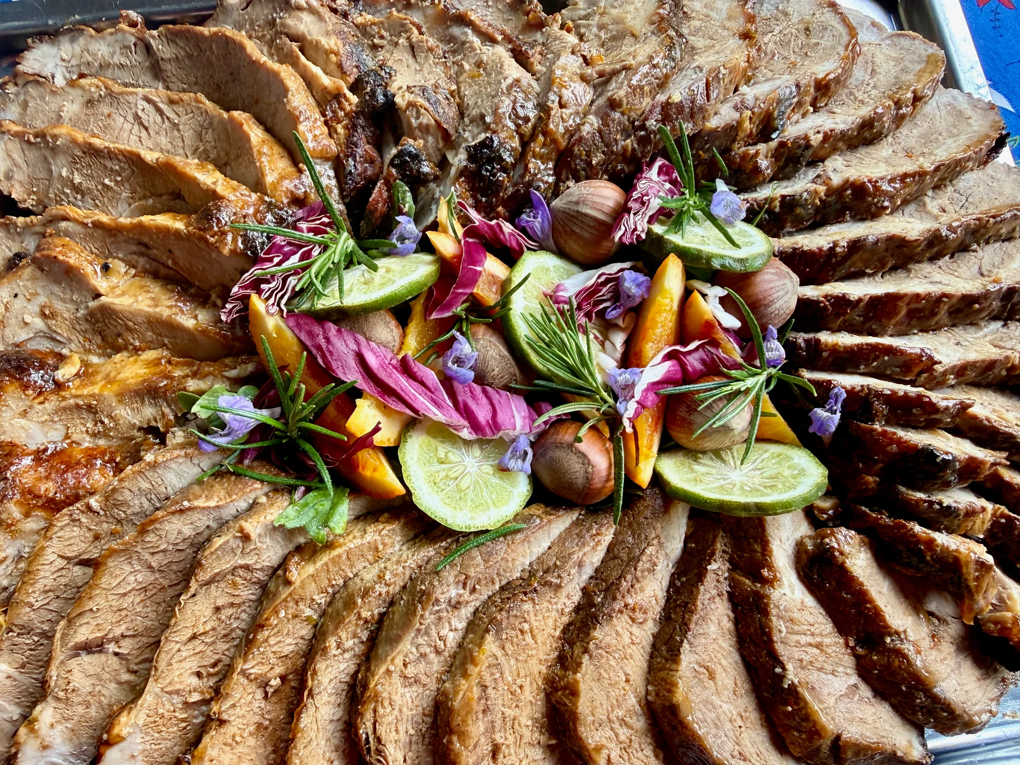 A platter of sliced roast meats garnished with herbs, citrus, and edible flowers, prepared by a local chef at Moulin à Rêves