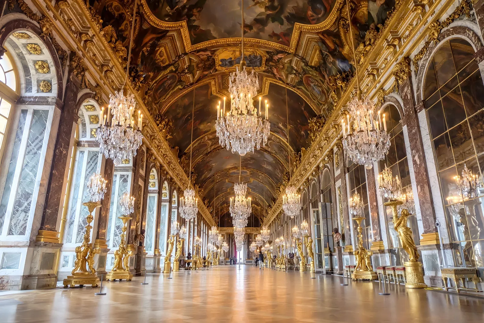 The Hall of Mirrors at the Palace of Versailles — gilded statues, crystal chandeliers, and the painted ceiling by Le Brun