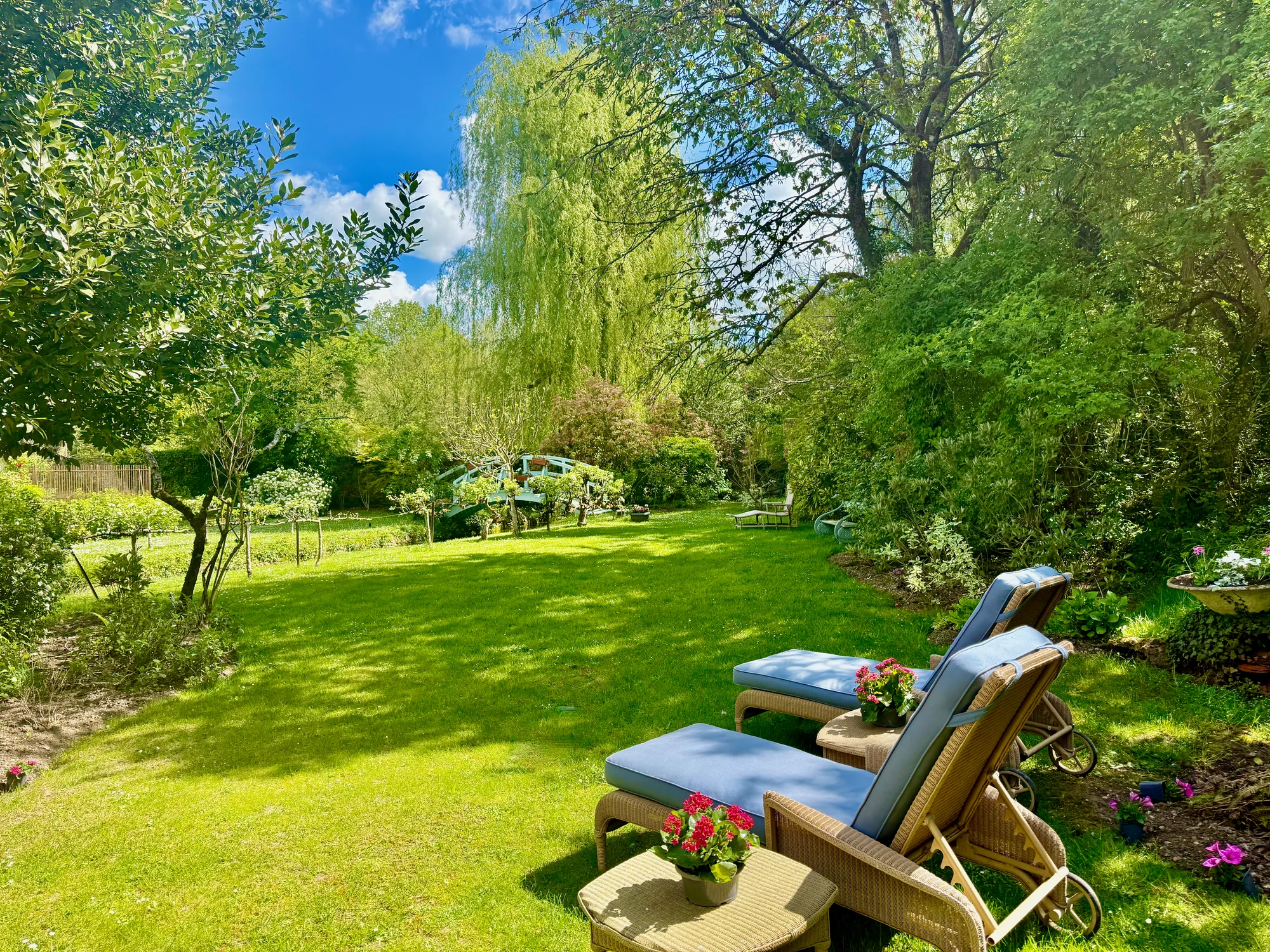 Wicker chaise lounges on the sunlit garden lawn beneath a weeping willow at Moulin à Rêves