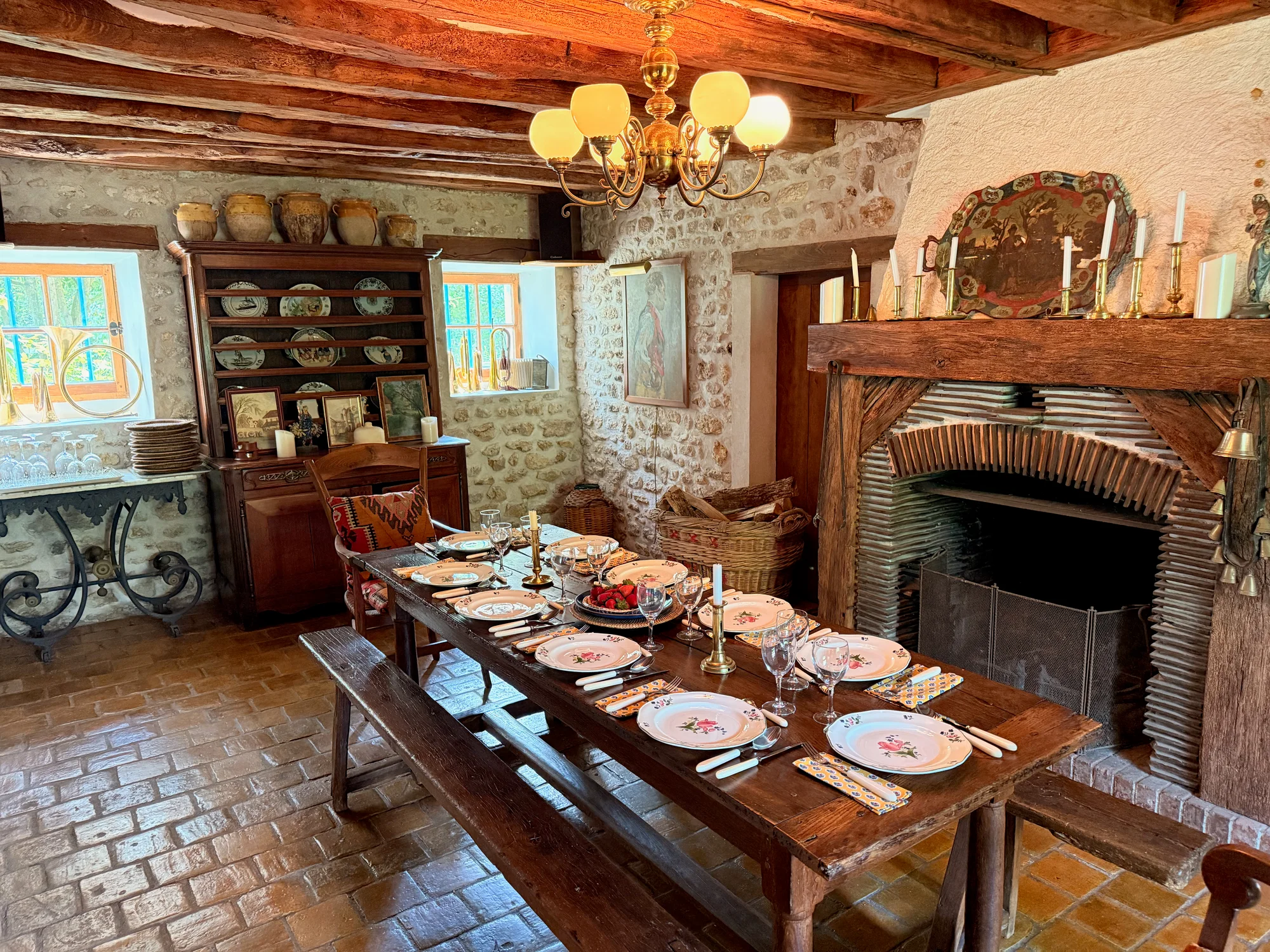 Formal dining room with a single long table set for ten beneath the beamed ceiling and stone fireplace