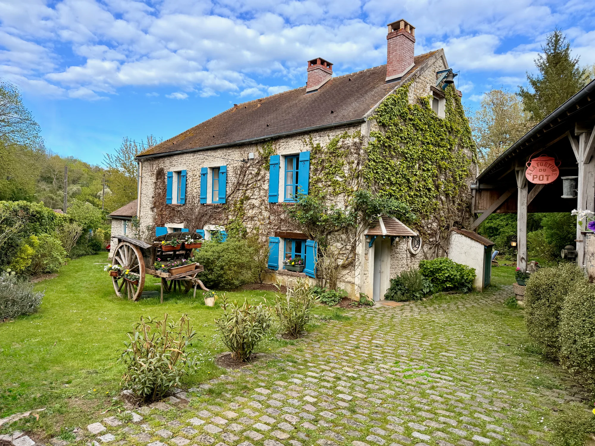 Le Moulin — stone facade with blue shutters and the antique flower cart in the cobblestone courtyard