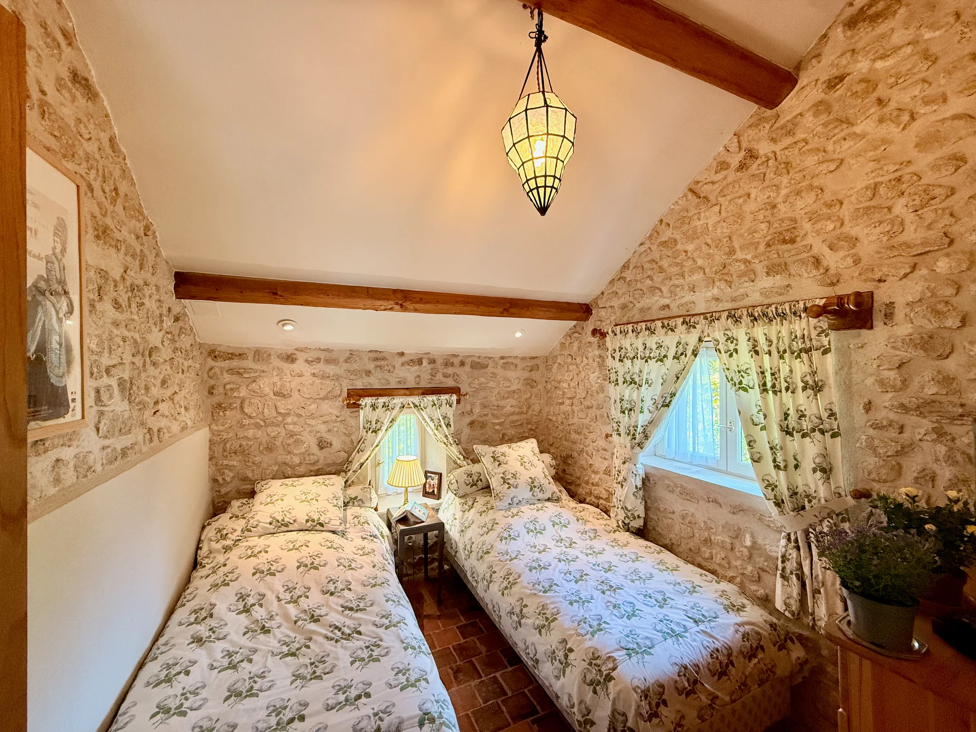 La Chambre de la Rivière — twin beds with stone walls and lantern light