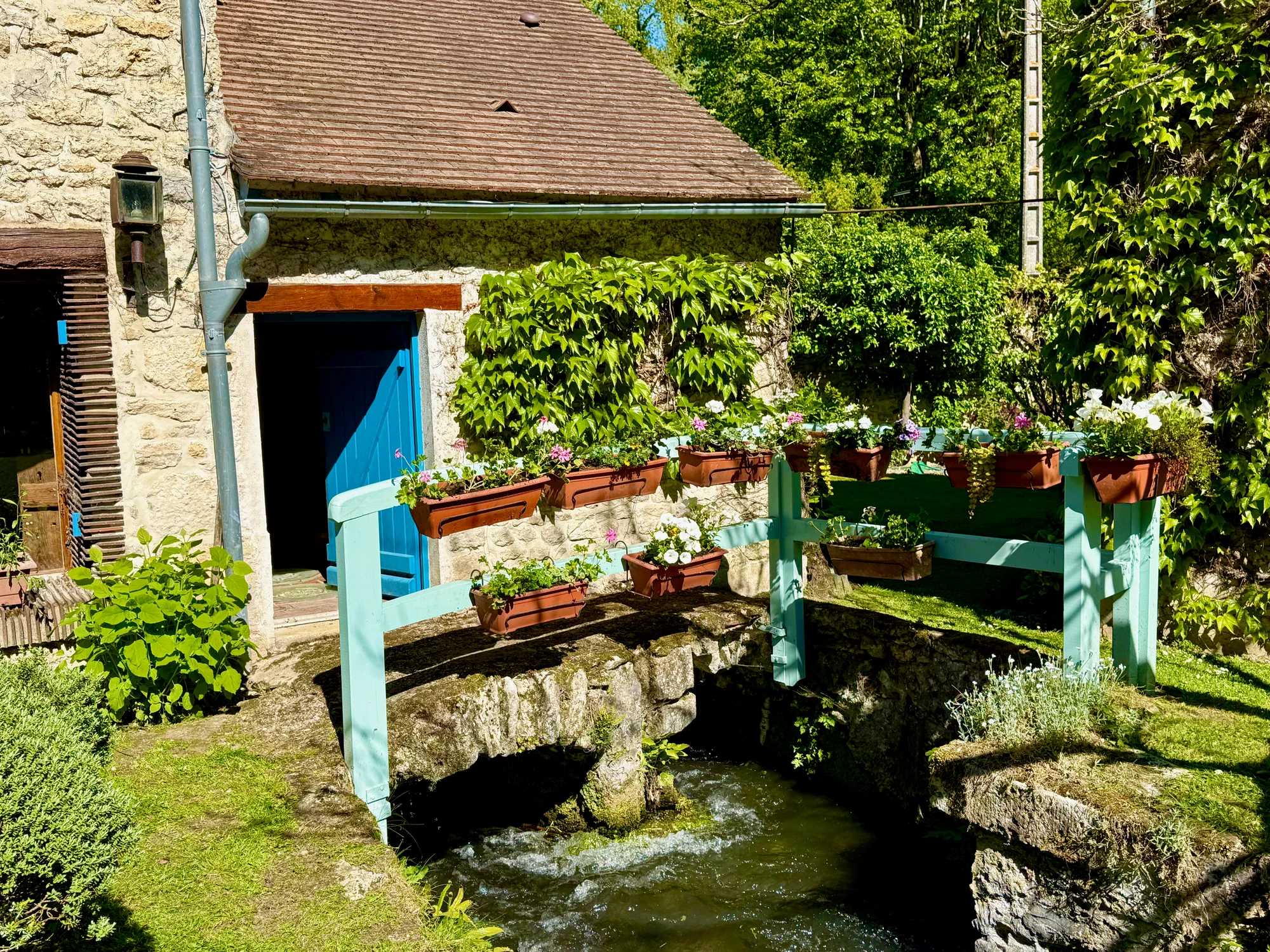 The Juine stream running beneath the flower-boxed footbridge at Le Moulin's blue door