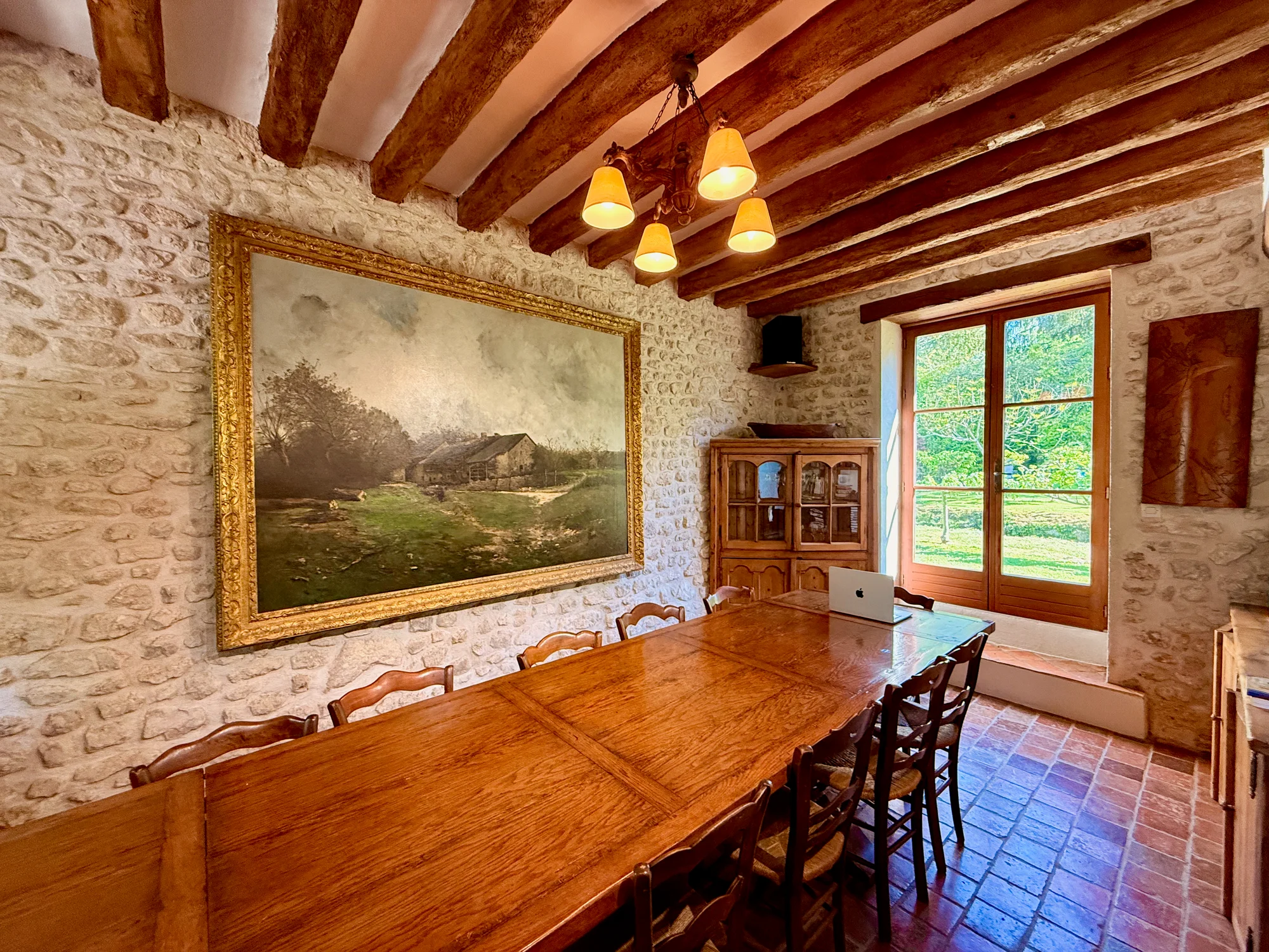 Dining room with grand landscape painting and stone walls at La Maison de la Rivière