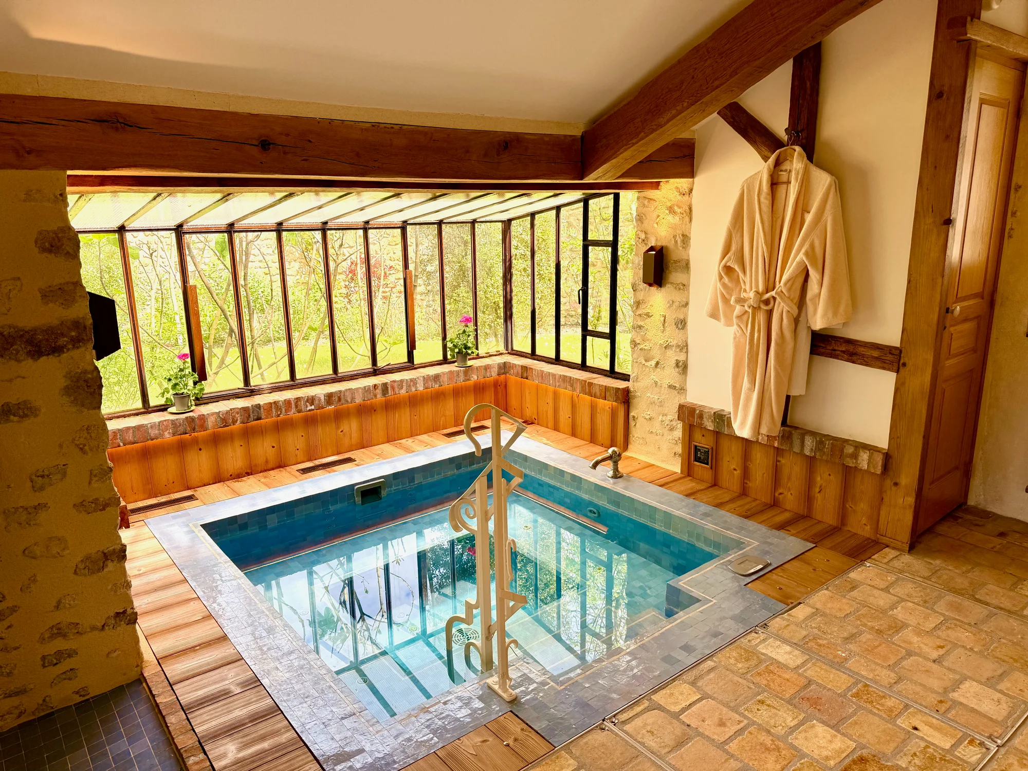 The glass-enclosed solarium jacuzzi with a robe and stone walls at Moulin à Rêves